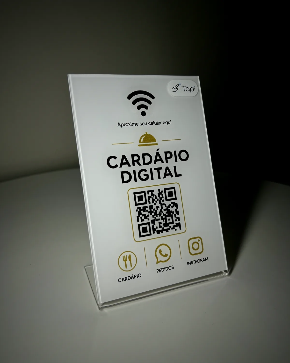 Plaquinha de acrílico branco 'Cardápio Digital' com QR code dourado, sobre uma mesa